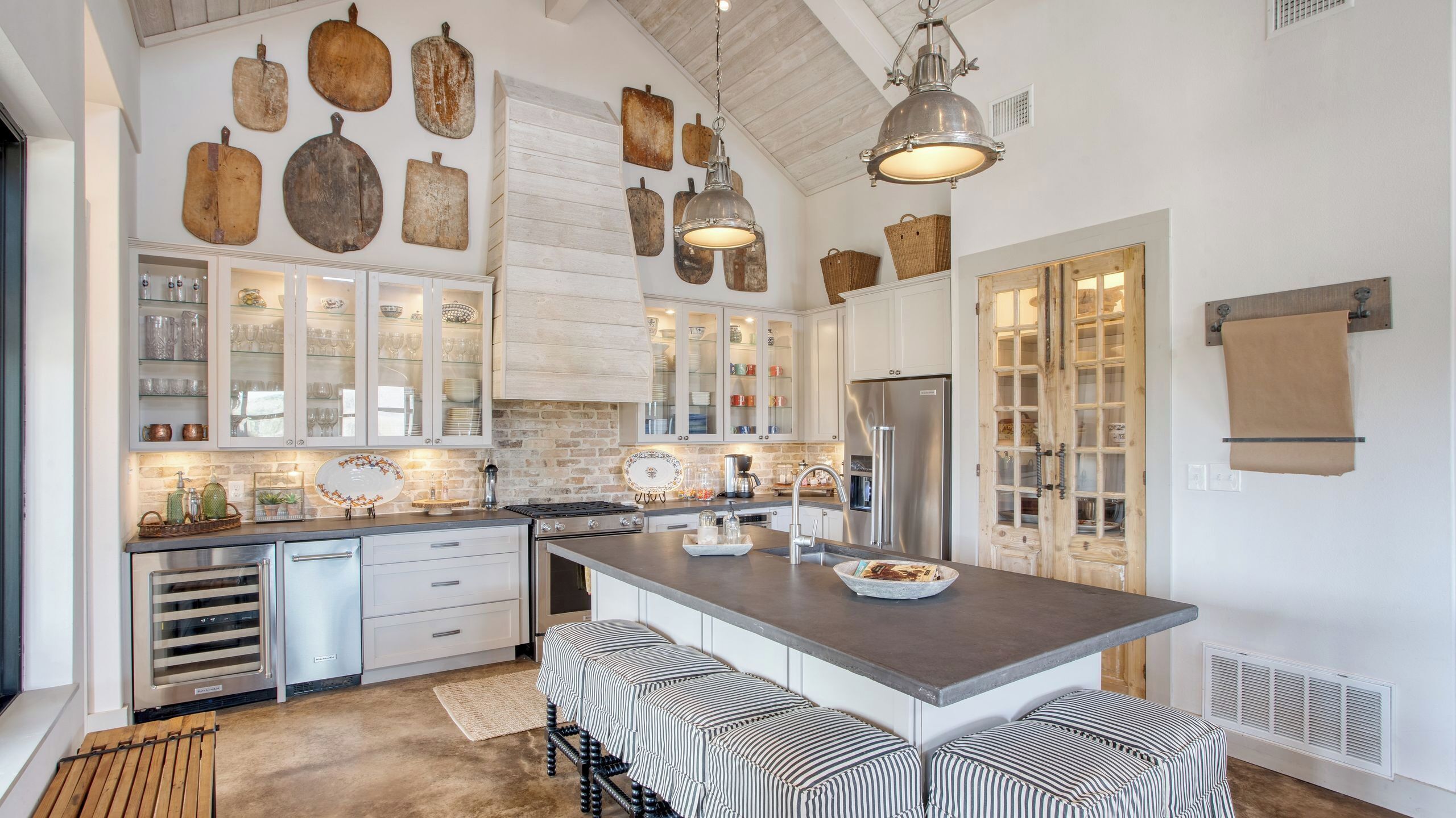 Een moderne keuken met witte kasten, een centraal eiland met gestreepte krukken en rustieke wanddecoraties.