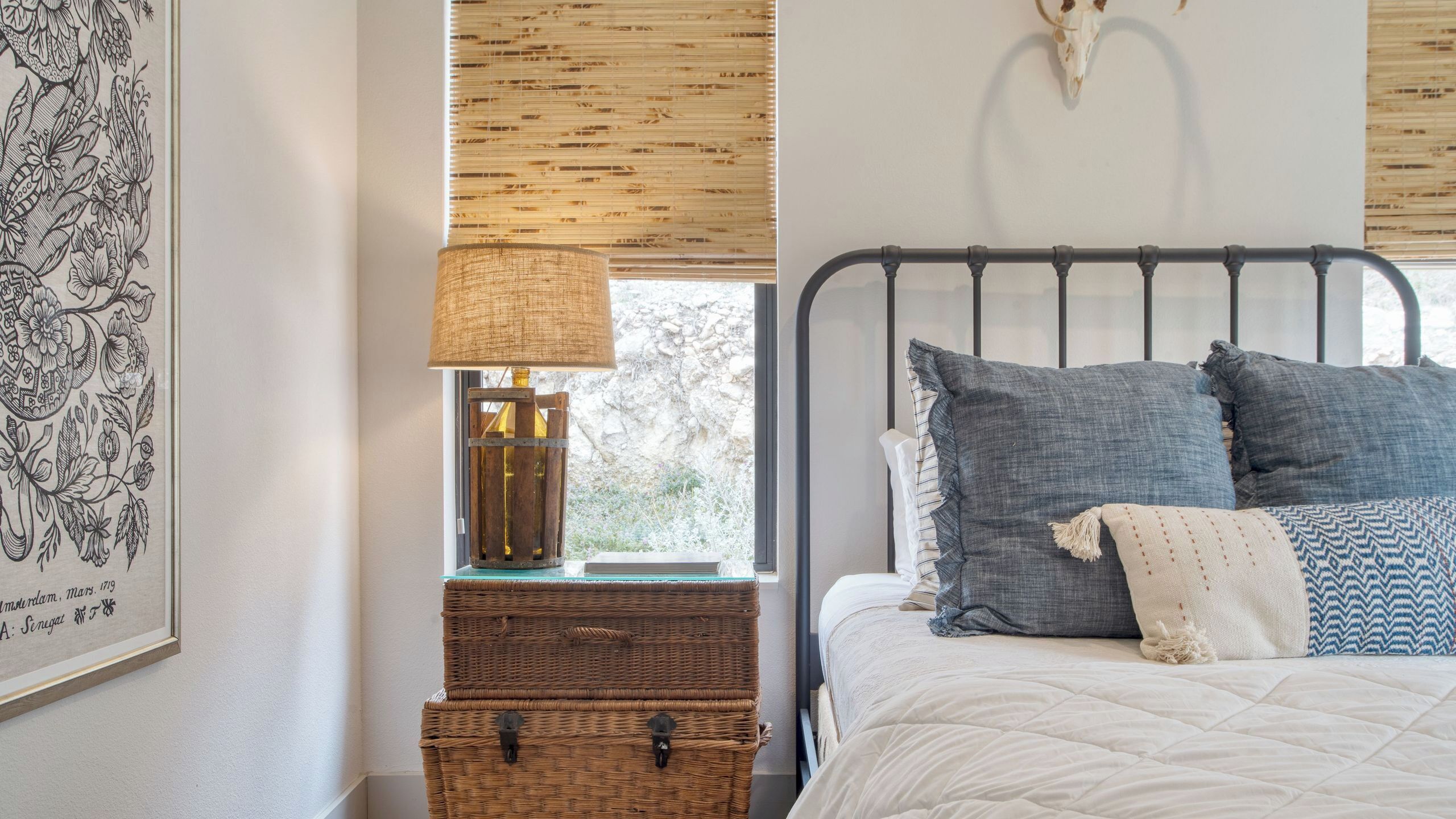 A bed with multiple pillows, a lamp, a framed picture, and a window with a view of the outdoors.