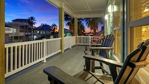 A covered outdoor area with wooden benches and tables, white railings, and a view of houses and palm trees in the background. - Jones N by the Beach by Avantstay Walk to Beach (Port Aransas)