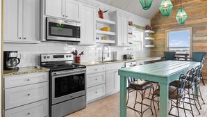 Une cuisine moderne avec des meubles blancs, des appareils en acier inoxydable et une table à manger turquoise, accompagnée de tabourets de bar.