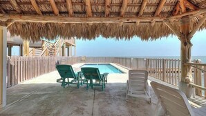Un espace extérieur abrité avec une piscine, deux chaises vertes et une clôture en bois donnant sur la mer.