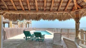 Un espace extérieur abrité comprenant une piscine, des chaises vertes et une terrasse en bois.