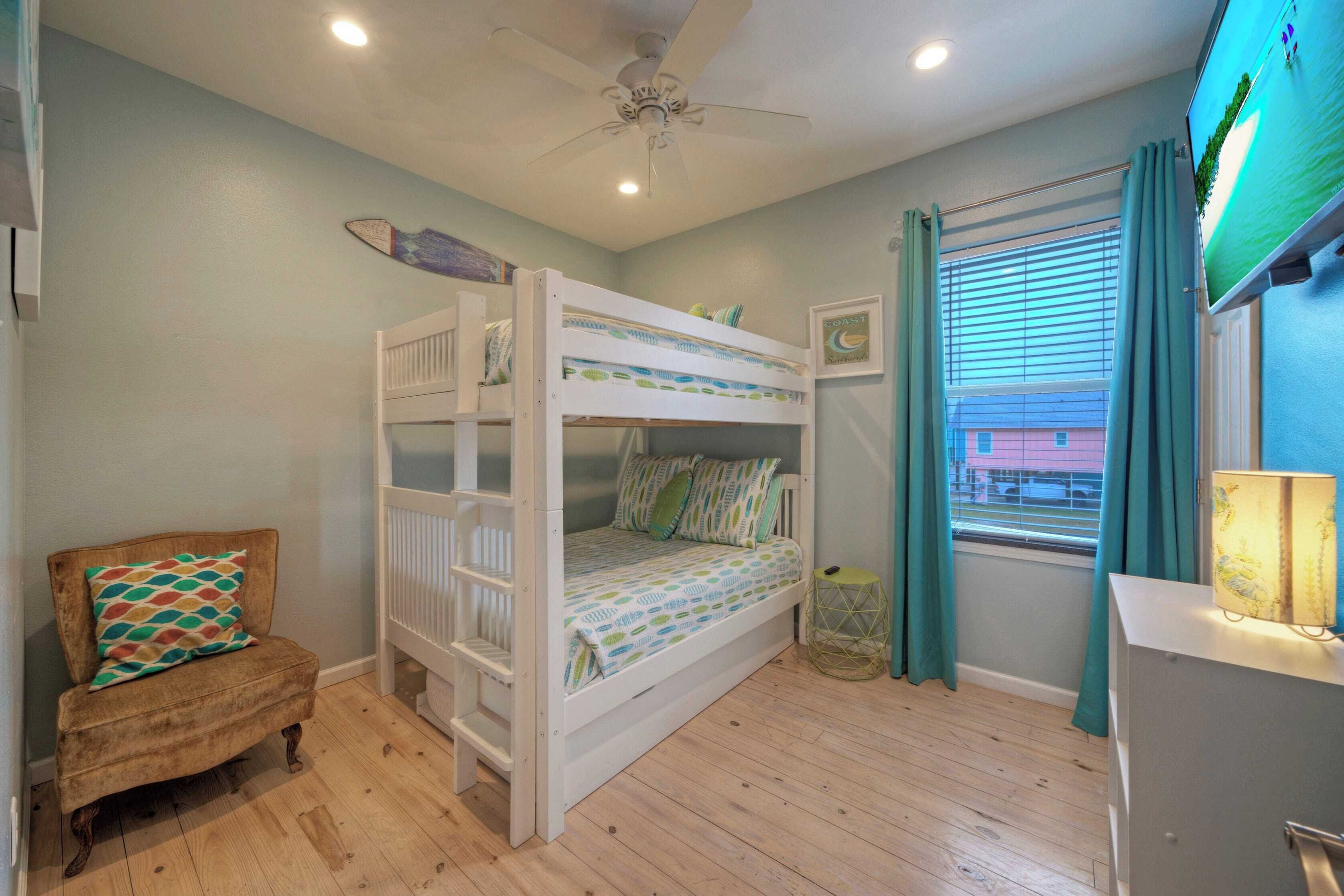 A bunk bed with a ceiling fan, a small armchair, and a window with curtains.
