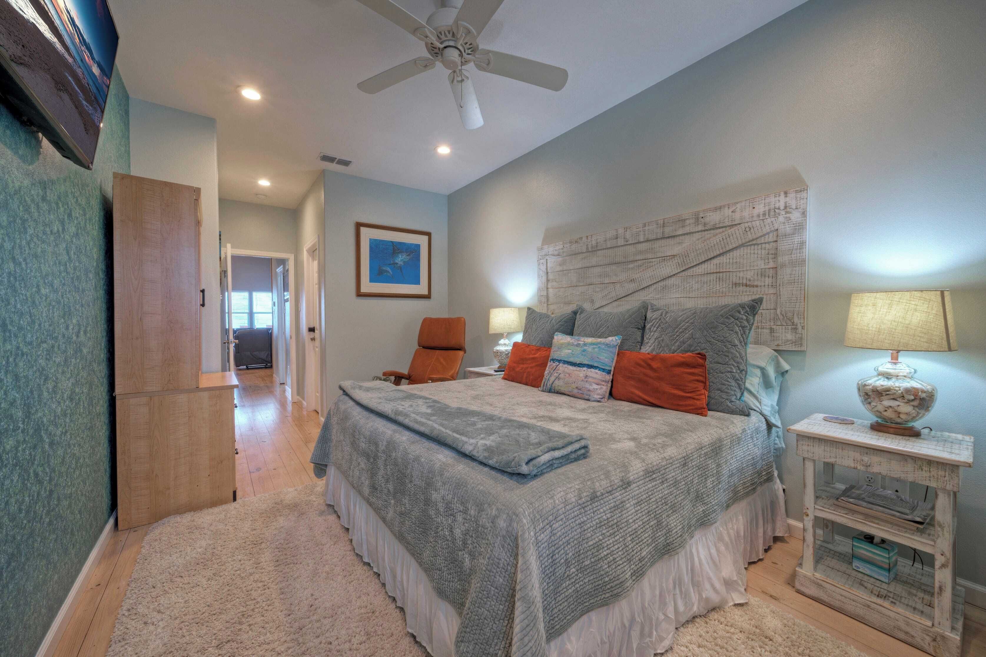 A bedroom with a bed, a nightstand, a ceiling fan, and a door leading to another room.