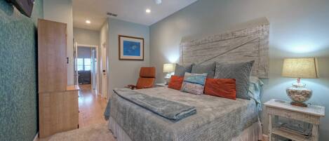 A bedroom with a bed, a nightstand, a ceiling fan, and a door leading to another room.