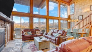 Un salon spacieux avec des canapés en cuir, une table basse et de grandes fenêtres offrant une vue sur les montagnes.