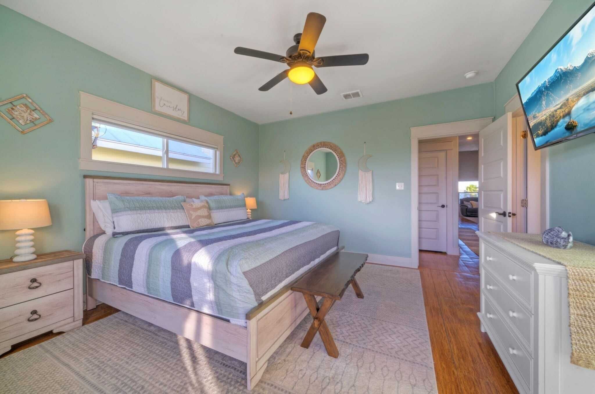 A bedroom with a bed, bedside tables, a ceiling fan, a window, a mirror, and a dresser.