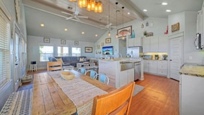 A spacious kitchen with a central island, a dining area with a wooden table, and a living room with a sofa and TV. - Nature Preserve View, Shared Pool, Outdoor Living Casa Pescadora by Avantstay (Port Aransas)
