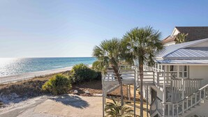 A beachfront property with a white building, a wooden deck, and a palm tree.