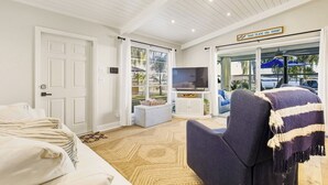 Een moderne woonkamer met een televisie, een bank en een fauteuil. Er is een deur met een bordje erboven.