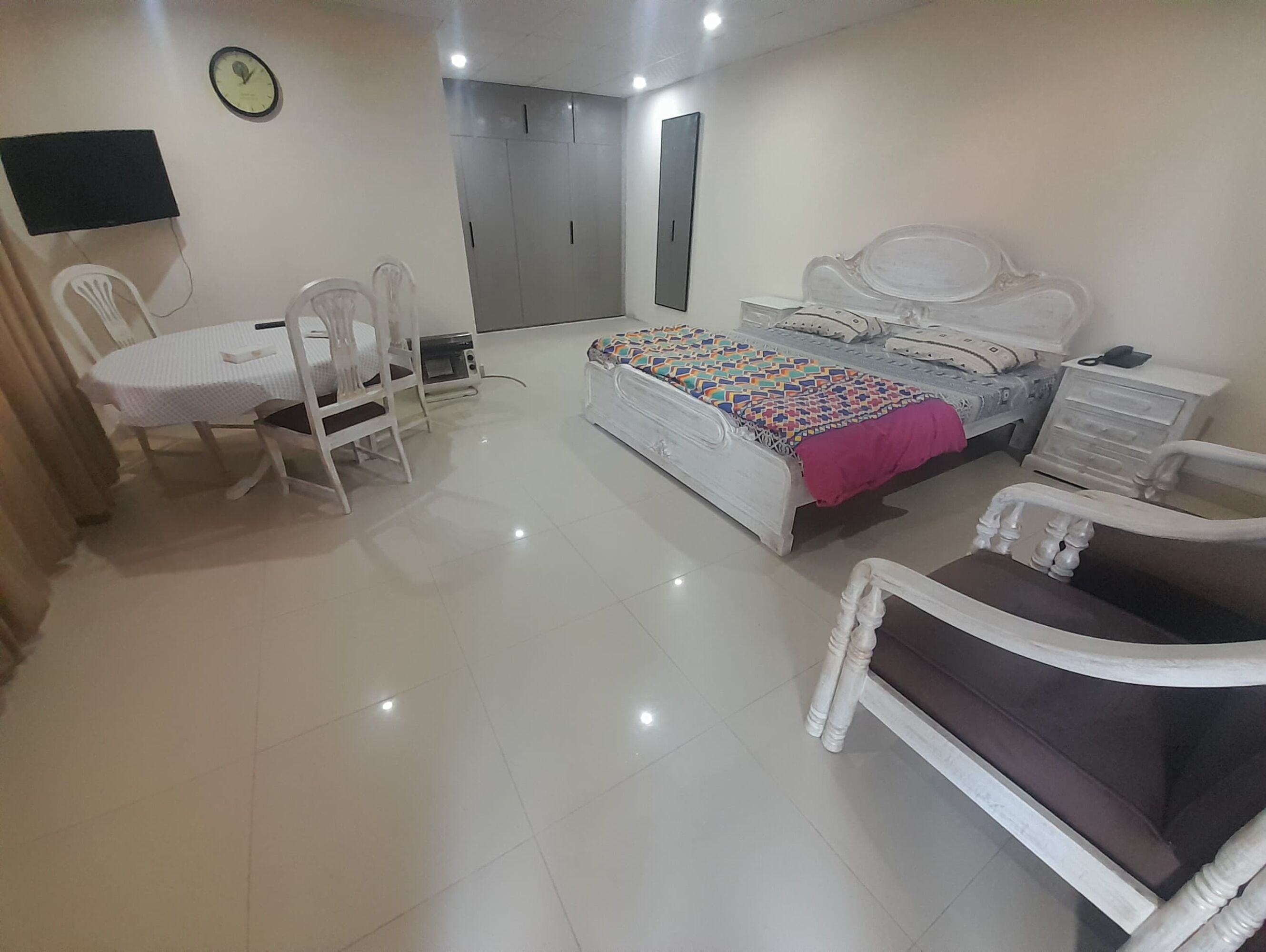 A bedroom with a bed, a desk, a chair, a TV, and a wardrobe.
