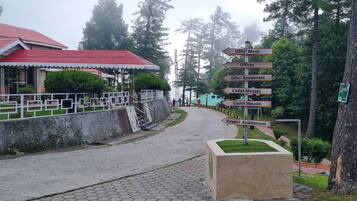 Un sendero conduce a un edificio con tejado rojo y un cartel indicador que muestra direcciones a varias instalaciones, incluyendo 'Offrs' Mess', 'Offrs' Residences', 'Cadet Messes', 'Cadet Houses' y 'Kayani Auditorium'.