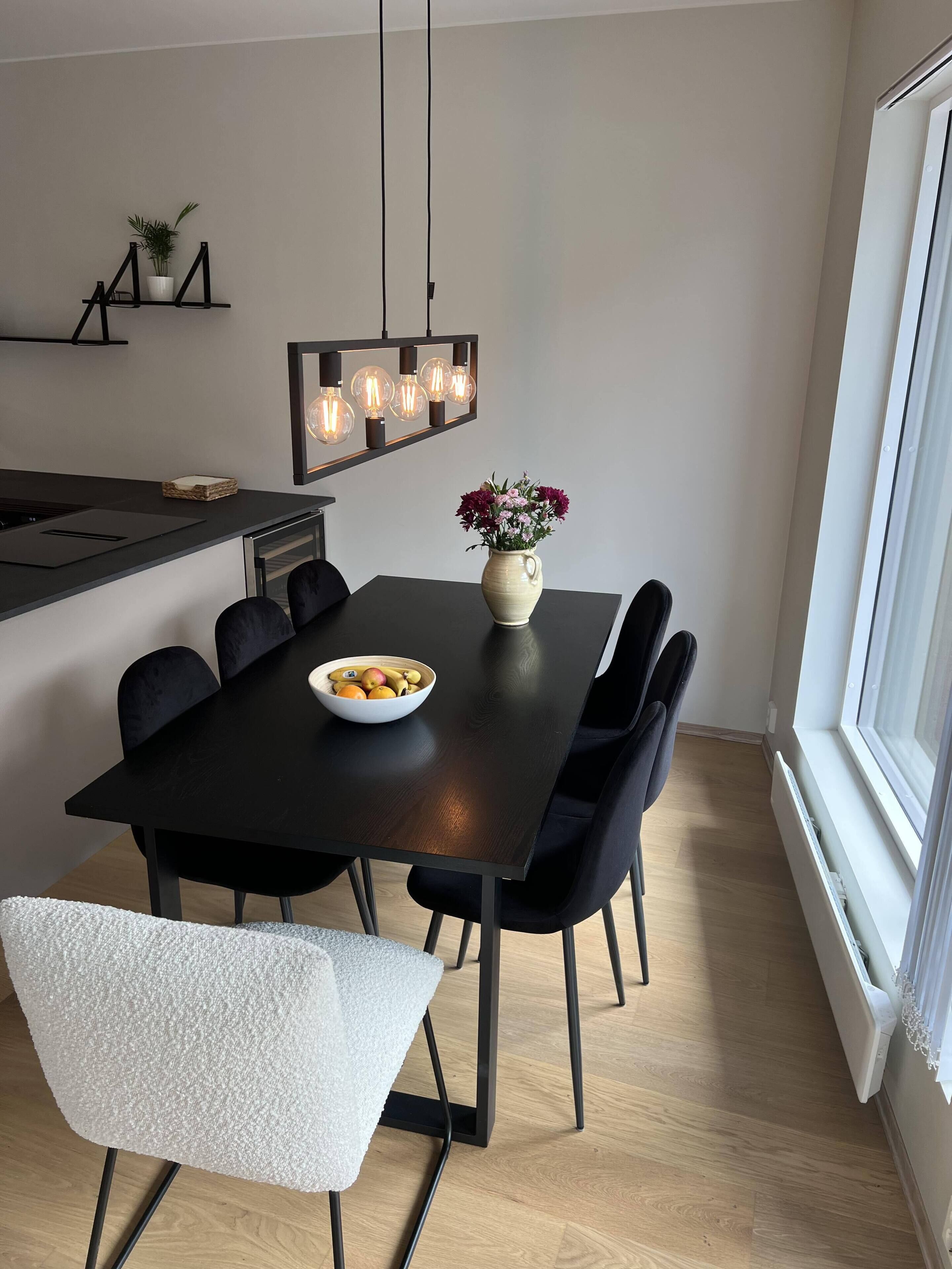 Een moderne eethoek met een zwarte tafel, zes stoelen, een vaas met bloemen en een schaal fruit.