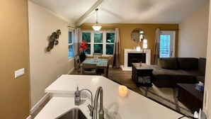 A modern kitchen with a central island, a dining area with a table and chairs, a fireplace, and a living room with a sofa and a coffee table. - Beautiful Laguna 2 Bedroom Condo (Laguna Niguel)