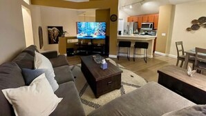 A living room with a sofa, a coffee table, and a TV. There is a kitchen area with a bar and a dining table. - Beautiful Laguna 2 Bedroom Condo (Laguna Niguel)