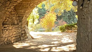 Un arco de piedra que da acceso a un jardín con árboles y un sendero.