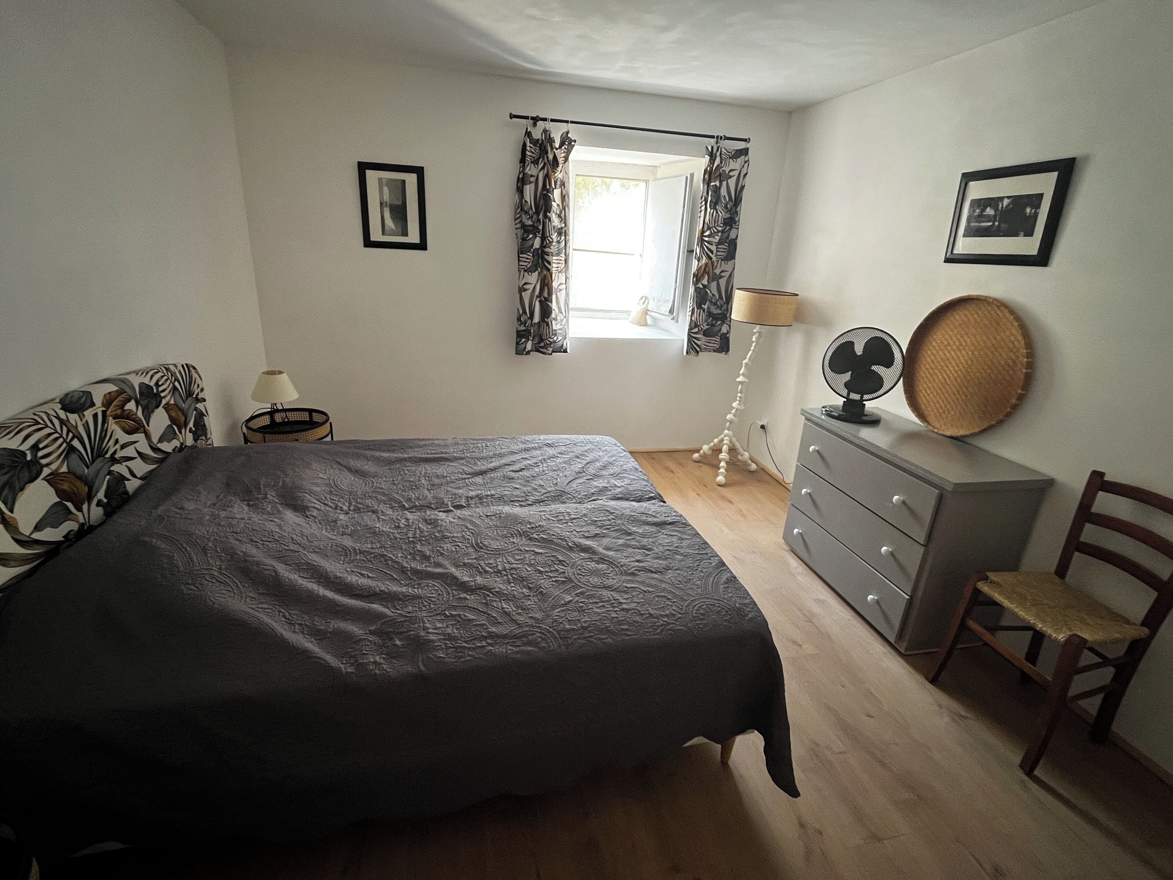 Een slaapkamer met een bed, een dressoir, een stoel, een lamp en een raam met gordijnen.