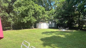 A grassy backyard with a metal chair, a shed, and a table. - Edward's Place ~ Family Retreat Near Downtown & Oaklawn (Hot Springs)