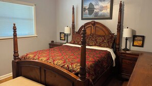 A four-poster bed with a red and gold patterned bedspread, two bedside tables with lamps, a bench, and a framed picture on the wall. - Edward's Place ~ Family Retreat Near Downtown & Oaklawn (Hot Springs)