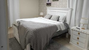 Un dormitorio con cama, una mesita de noche con lámpara, cómoda con cajones y un equipo de aire acondicionado en la pared.