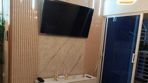 Una sala de estar moderna con un televisor de pantalla plana montado en una pared de mármol, una consola blanca con detalles dorados y una mesa de centro redonda con objetos decorativos.