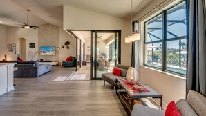 A spacious living area with a large window, a sofa, a coffee table, and a dining area visible through an open door. - Special Offer Villa Felicity - river access, pool & spa, quiet, charming (Cape Coral)