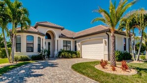 A two-story house with a tiled roof, a garage, and a landscaped driveway with palm trees. - Special Offer Villa Felicity - river access, pool & spa, quiet, charming (Cape Coral)