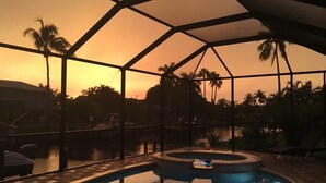 A swimming pool with a glass enclosure, surrounded by palm trees and a sunset view. - Special Offer Villa Felicity - river access, pool & spa, quiet, charming (Cape Coral)