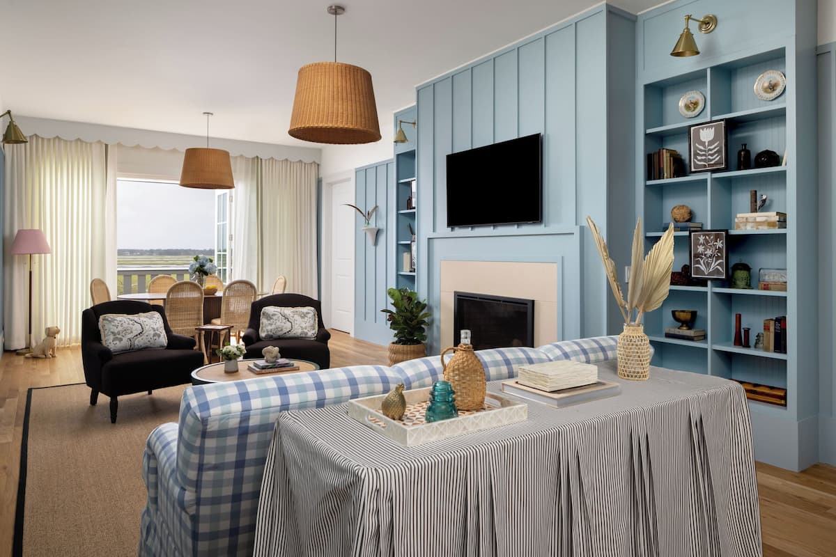 A living room with a checkered sofa, a coffee table with decorative items, a television mounted on the wall, and a bookshelf with various objects.