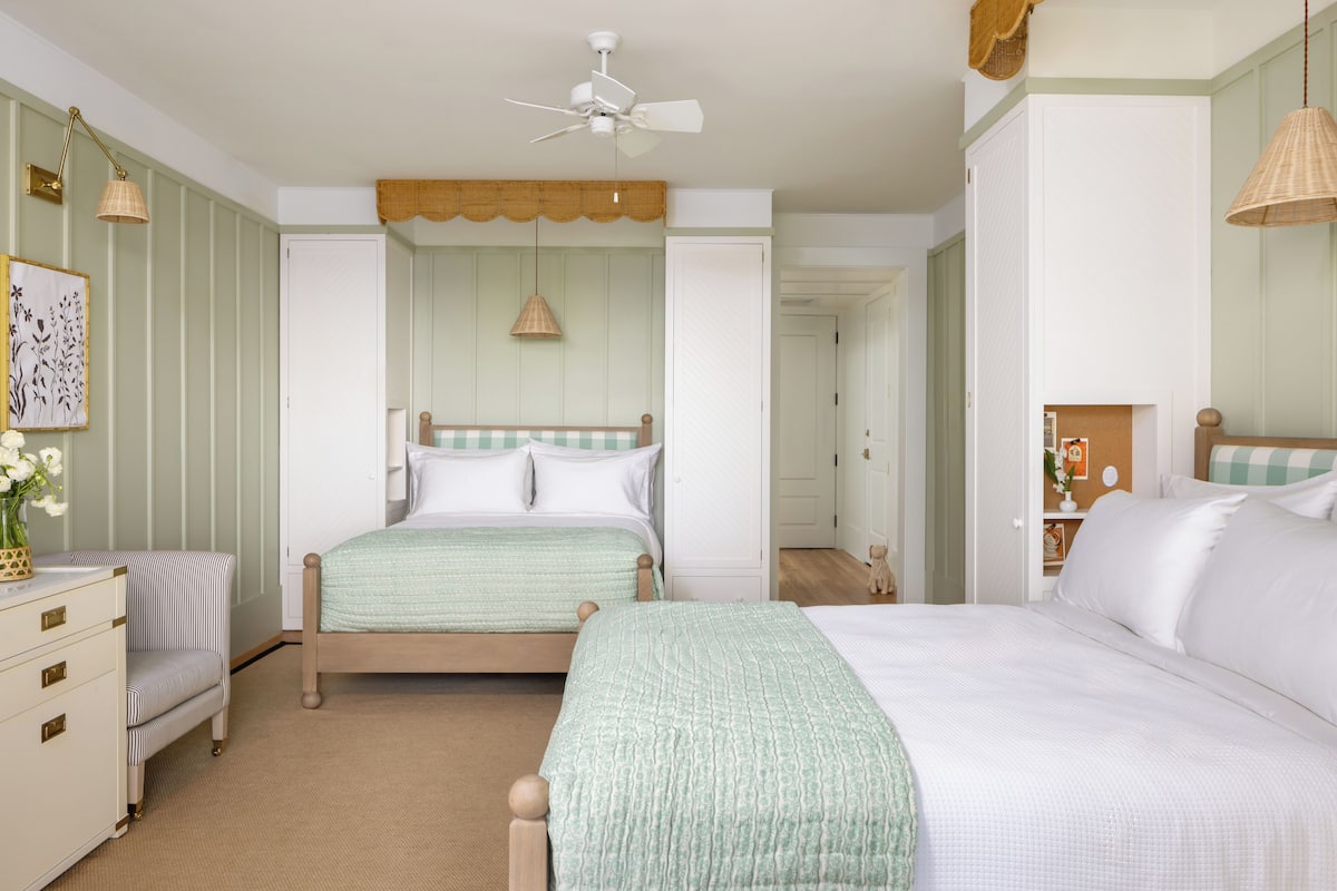 A bedroom with two beds, a dresser, a chair, and a ceiling fan.