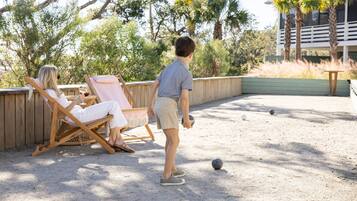A person playing croquet on a sandy court with a wooden fence and palm trees in the background.