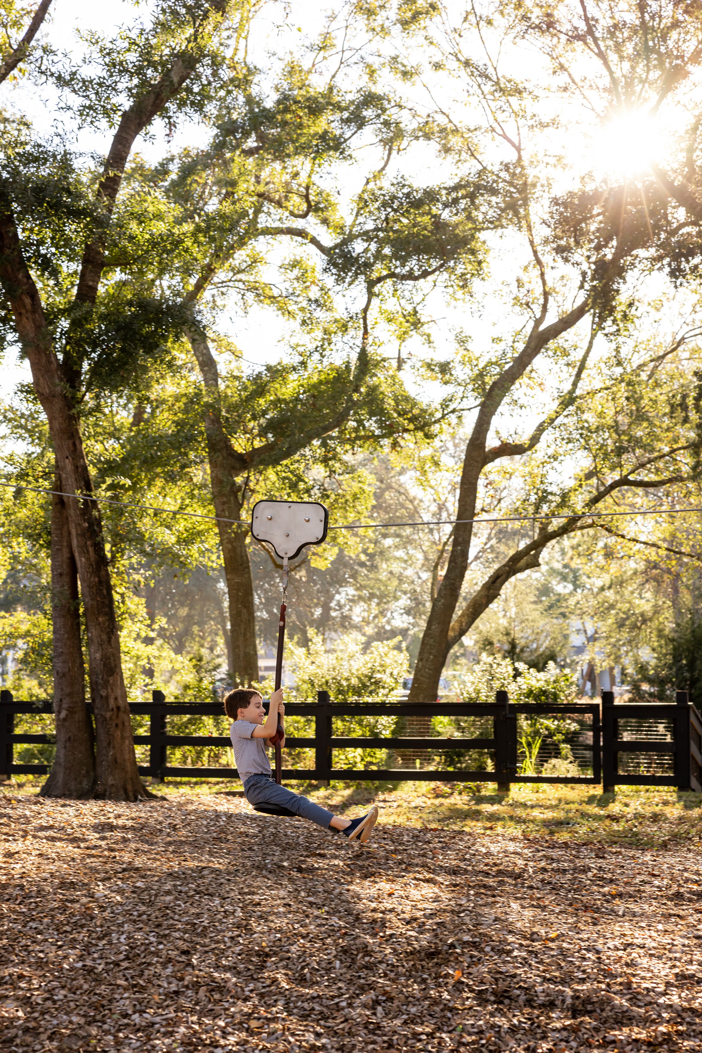 A person swinging on a swing in a park with trees and a wooden fence in the background.