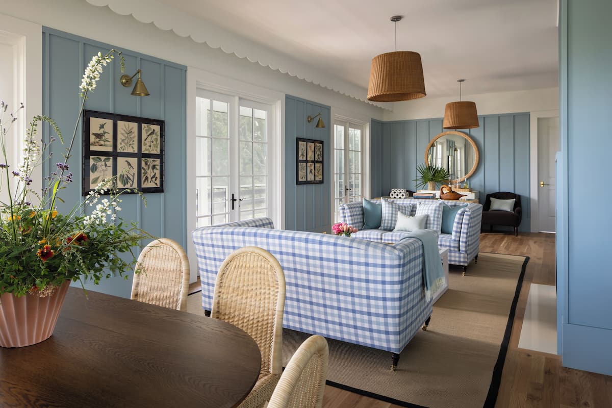 A room with a checkered sofa set, wicker chairs, a dining table, and a large mirror.