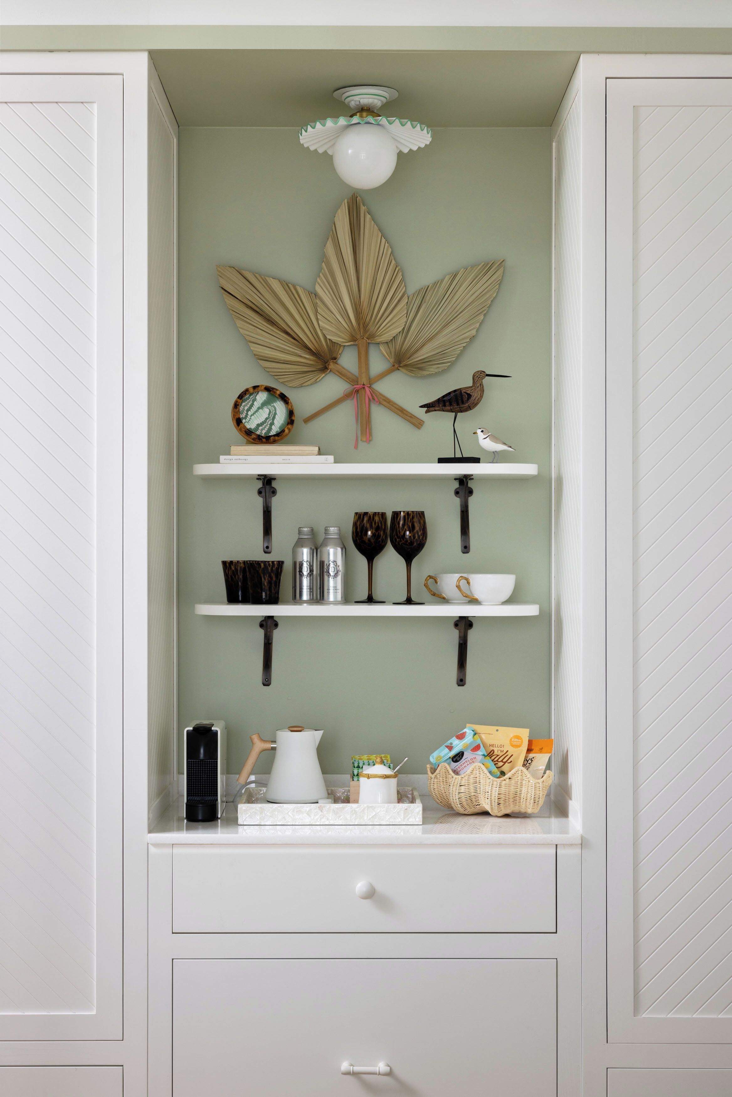 A kitchen with white cabinetry, a leaf decoration, and shelves with kitchenware.