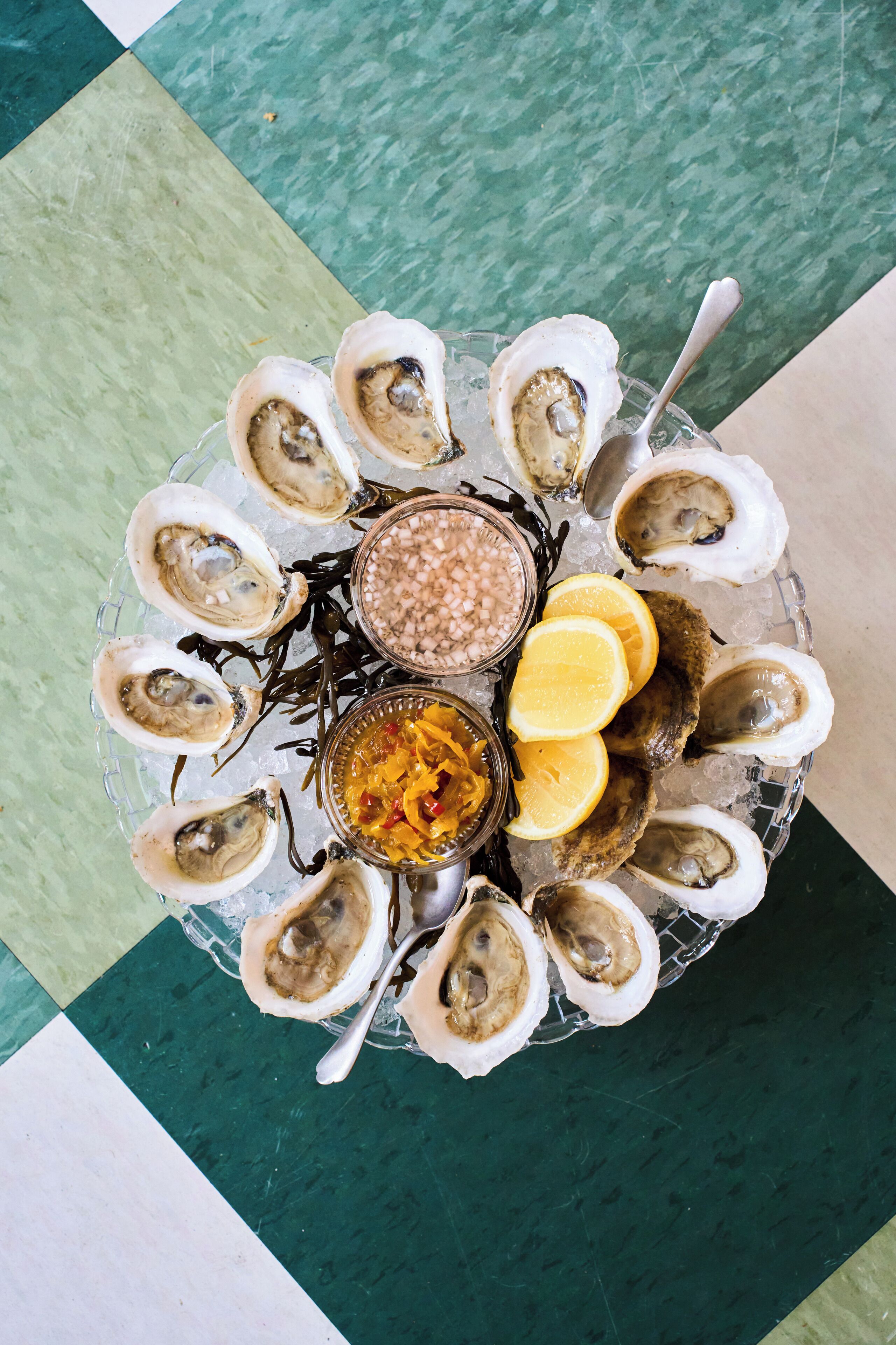 A plate of oysters with lemon wedges and two sauces on a bed of ice.