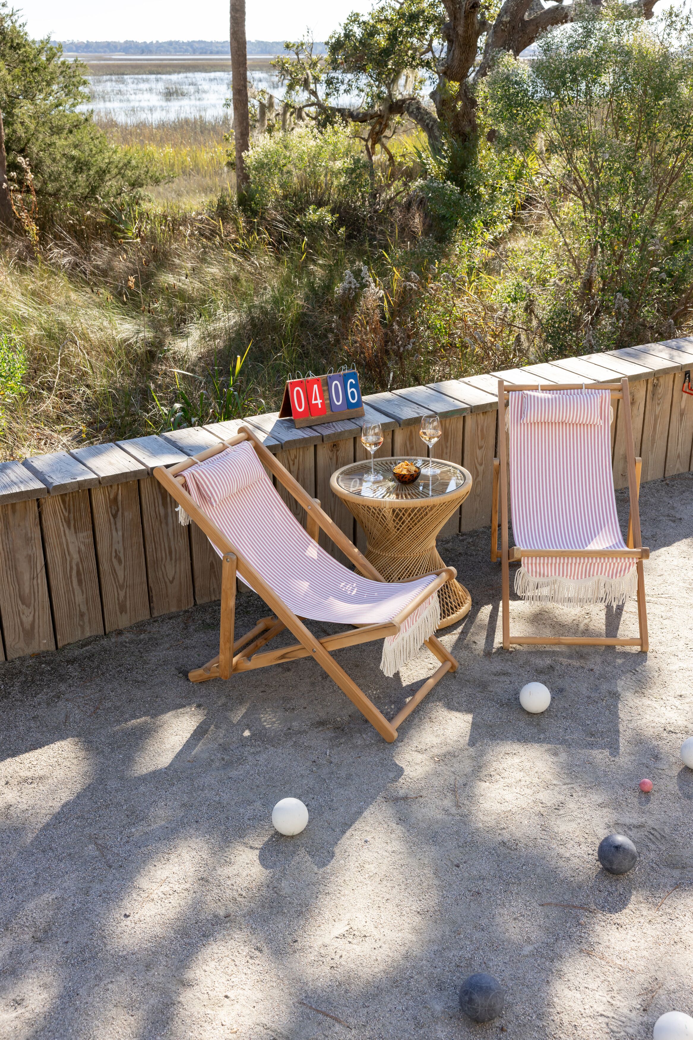 Deux fauteuils à rayures, une petite table ronde avec un saladier et des verres à vin, et une clôture en bois portant une inscription indiquant une date.