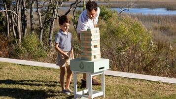 Twee personen spelen Jenga in een open setting, met een waterpartij en bomen op de achtergrond.