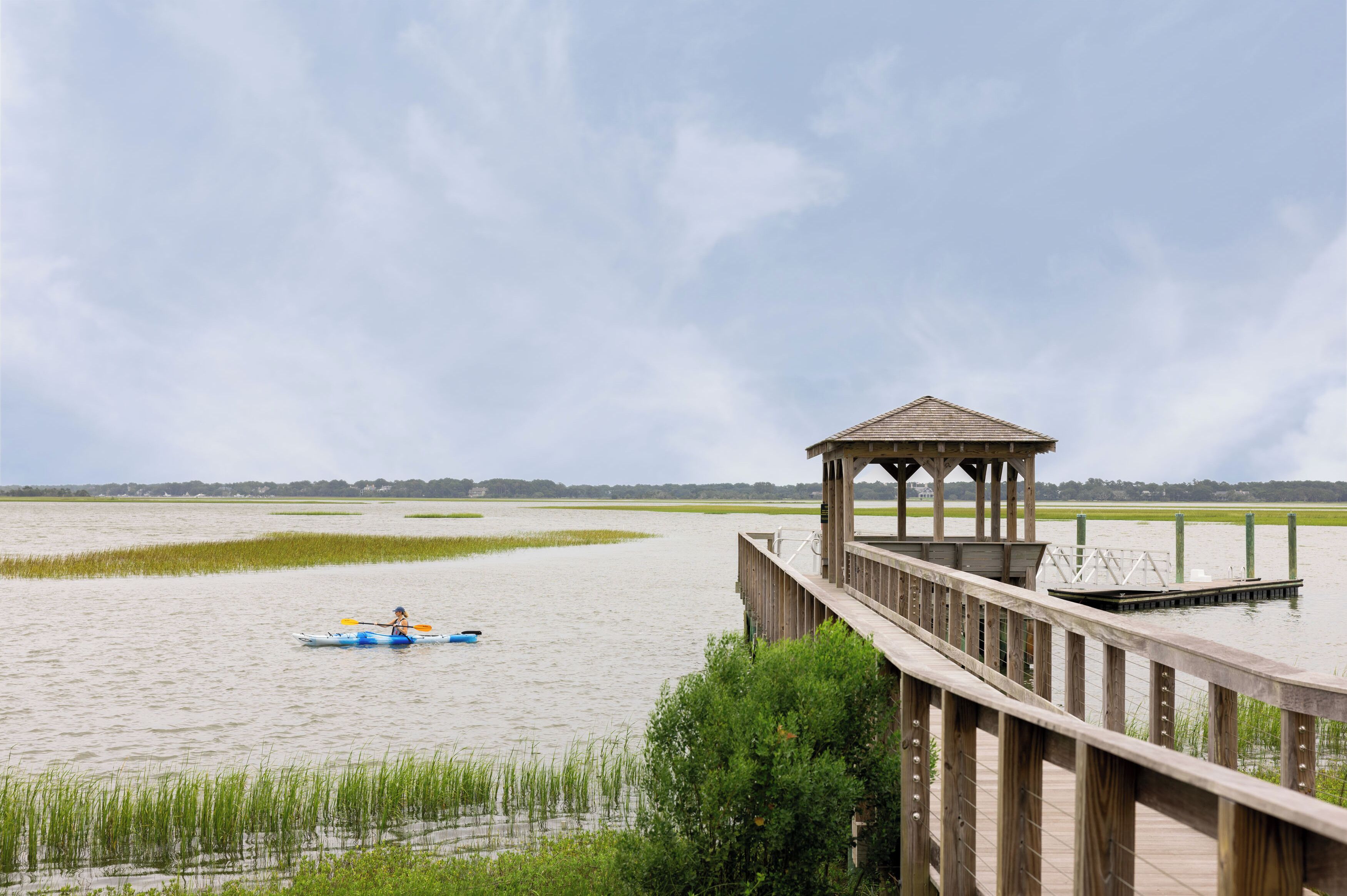 A wooden pier leading to a gazebo over a calm water body with a person kayaking.