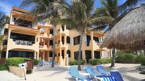 A multi-story hotel with balconies, palm trees, and beach chairs. - Relax in Your Private Beachfront Retreat, Surrounded by Breathtaking Ocean Views (Akumal)