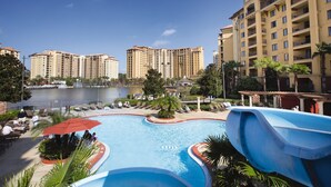 Zona de piscina en un resort, con tobogán de agua, sillas de descanso y vistas a edificios altos.