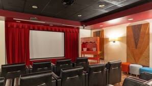 A theater room with black leather chairs, a white screen, red curtains, and a popcorn stand.