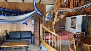 A room with a wooden staircase, a black leather sofa, a wooden dining table, and a large fish sculpture. - Living Life Dockside (Naval Air Station Key West)