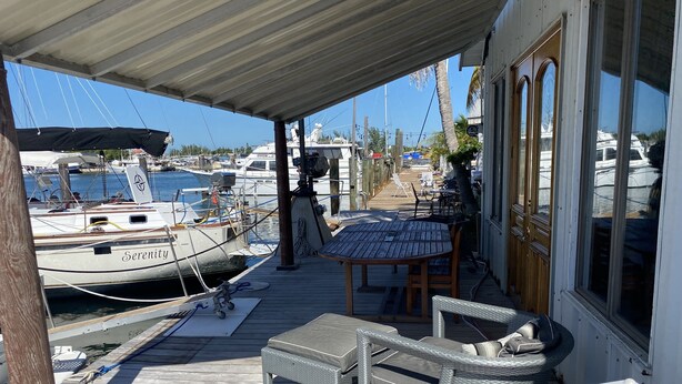 A covered outdoor area with a wooden deck, a table, and two wicker chairs. - Living Life Dockside (Naval Air Station Key West)