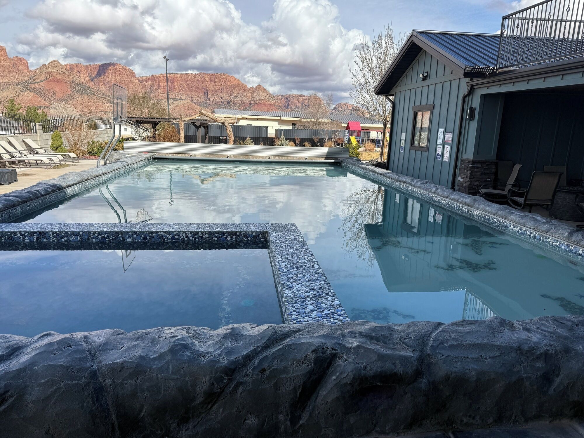 A swimming pool with a stone border, lounge chairs, and a mountain backdrop.