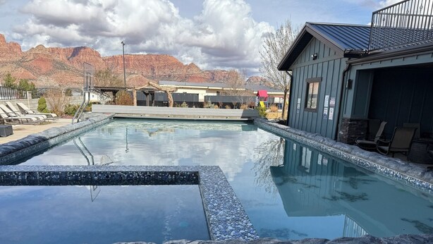 Ein Swimmingpool mit Steinrand, Liegestühlen und einem Berg im Hintergrund.