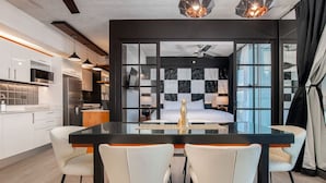A modern hotel room with a dining area featuring a glass table and white chairs.