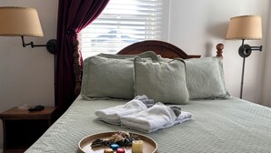 Ein ordentlich bezogenes Bett mit zwei Kissen, ein Nachttisch mit Lampe und ein Tablett mit Snacks und einer Kerze.