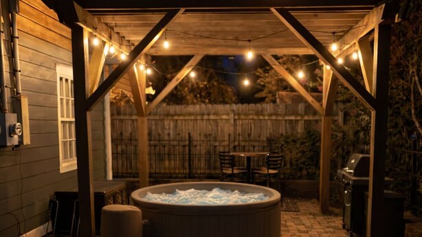 Eine Terrasse im Freien mit Whirlpool, Feuerstelle und Lichterketten.