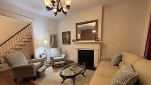 Ein Wohnzimmer mit Kamin, zwei Sesseln, einer Couch, einem Couchtisch und einem Kronleuchter.