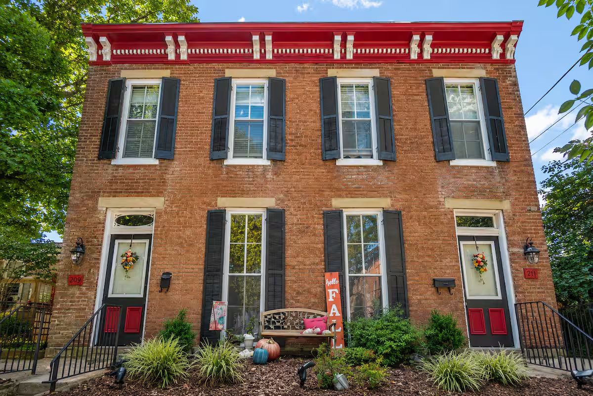 A two-story brick building with a red roof, black shutters, and a bench in front.